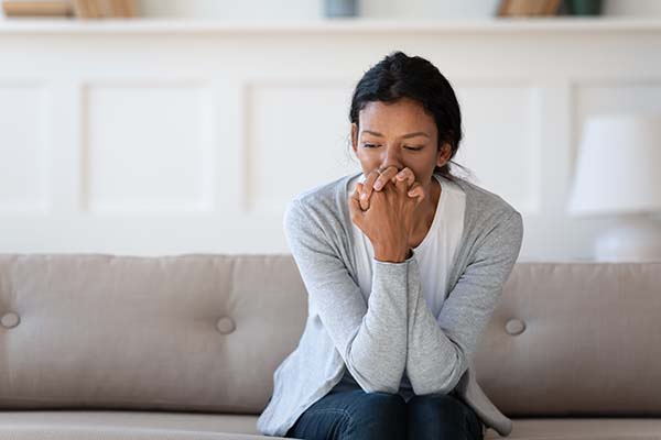 Worried young african american woman sitting on sofa, thinking of personal problems alone indoors, copy space. Unhappy mixed race lady feeling frustrated or nervous, suffering from loneliness.