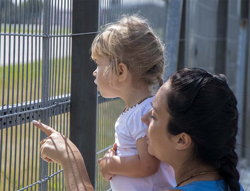 A woman and a child look into the distance through a fence with